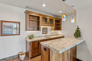 Kitchen with open shelves, brown cabinetry, light wood-type flooring, pendant lighting, and a peninsula