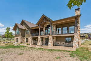 Rear view of house featuring a balcony, stone siding, a patio area, board and batten siding, and a chimney