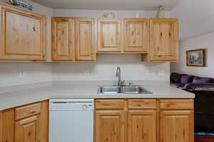 Kitchen featuring light brown cabinets, a sink, open floor plan, white dishwasher, and light countertops