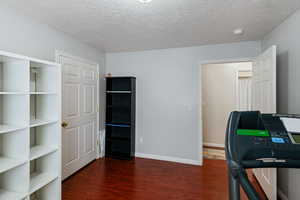 Exercise room with a textured ceiling, baseboards, and wood finished floors