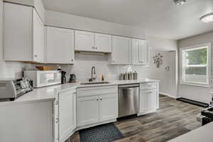 Kitchen featuring stainless steel dishwasher, light countertops, white microwave, decorative backsplash, and white cabinetry