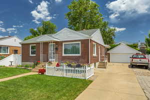 Bungalow featuring a detached garage, an outbuilding, brick siding, and roof with shingles