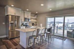 Kitchen featuring a center island with sink, dark wood finished floors, light countertops, appliances with stainless steel finishes, and backsplash