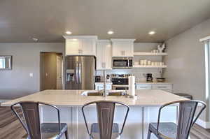 Kitchen featuring a center island with sink, backsplash, dark wood finished floors, white cabinetry, and stainless steel appliances
