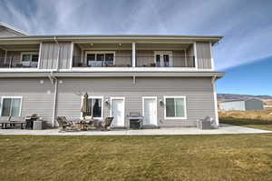 Back of property featuring board and batten siding,  a yard, a balcony, and a patio