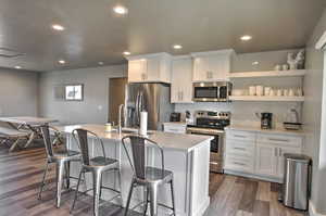 Kitchen featuring dark wood-style floors, a kitchen island with sink, a sink, appliances with stainless steel finishes, and white cabinetry