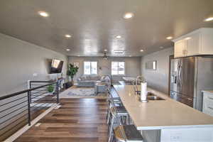 Kitchen featuring dark wood-style floors, a sink, a large island, stainless steel refrigerator with ice dispenser, and white cabinetry
