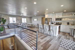 Kitchen with light wood finished floors, open floor plan, light countertops, appliances with stainless steel finishes, and white cabinets