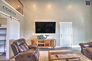 Living room with visible vents, a barn door, baseboards, and wood finished floors