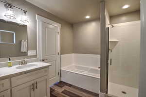 Primary bath suite. Full bathroom featuring a garden tub, recessed lighting, a stall shower, wood finished floors, and vanity