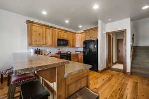 Kitchen featuring tasteful backsplash, a kitchen breakfast bar, light wood-type flooring, a peninsula, and black appliances