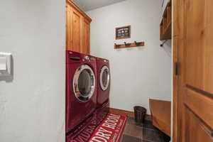 Clothes washing area with tile patterned floors, baseboards, washing machine and clothes dryer, and cabinet space
