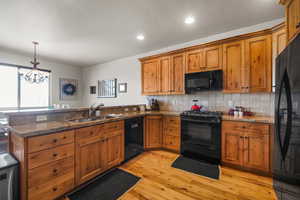 Kitchen featuring brown cabinetry, a peninsula, a sink, and black appliances