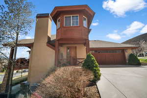 View of front facade featuring an attached garage, a shingled roof, driveway, and stucco siding