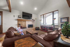 Carpeted living room featuring a tile fireplace, vaulted ceiling with beams, and visible vents