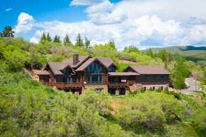 Rear view of property with a chimney, log exterior, a balcony, and stone siding