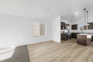 Kitchen featuring a center island, open floor plan, appliances with stainless steel finishes, and dark brown cabinets