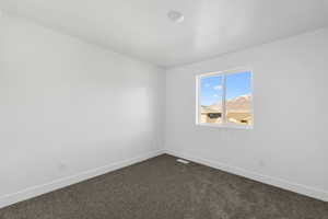 Spare room with visible vents, baseboards, dark colored carpet, and a textured ceiling
