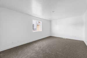 Unfurnished room featuring baseboards, dark carpet, and a textured ceiling