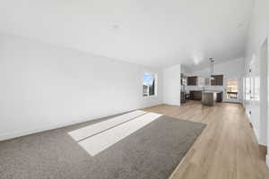 Unfurnished living room featuring baseboards, high vaulted ceiling, a sink, and light wood finished floors