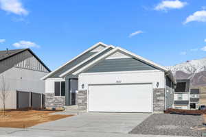 View of front facade featuring fence, stone siding, driveway, a mountain view, and a garage