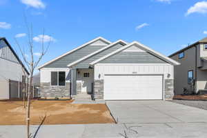 View of front of property with board and batten siding, stone siding, a garage, and concrete driveway