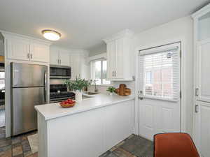 Kitchen featuring a peninsula, a sink, stainless steel appliances, light countertops, and white cabinets