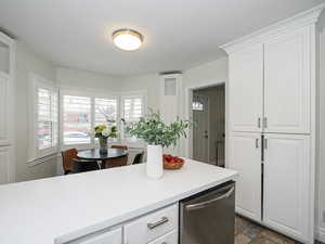 Kitchen featuring white cabinetry, light countertops, dishwasher, and stone finish flooring