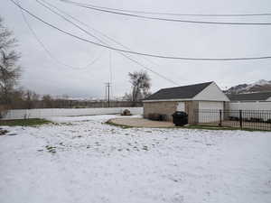 Snowy yard featuring an outdoor structure, a fenced backyard, and a detached garage