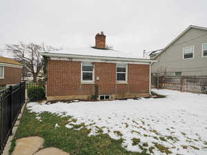 Snow covered property featuring brick siding, a fenced backyard, and a chimney