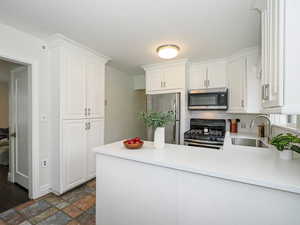 Kitchen with a sink, white cabinetry, appliances with stainless steel finishes, a peninsula, and light countertops