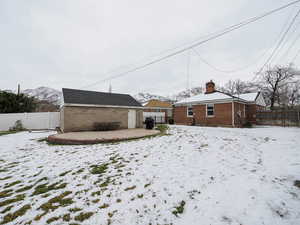 Snow covered property with brick siding, a chimney, a fenced backyard, an outdoor structure, and a mountain view