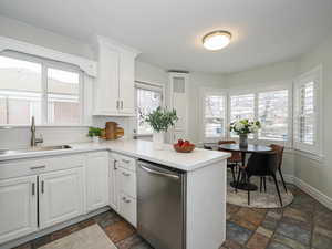 Kitchen featuring stainless steel dishwasher, stone tile flooring, a peninsula, and a sink