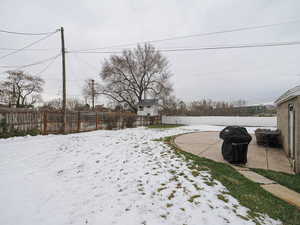 Yard layered in snow with a fenced backyard and a patio area