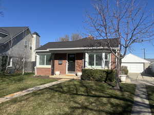 Bungalow-style home with an outdoor structure, fence, a front lawn, brick siding, and a shingled roof
