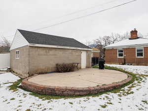 Snow covered house featuring a patio area, a shingled roof, a chimney, and fence