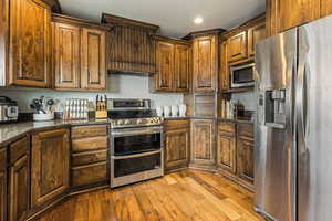 Kitchen with recessed lighting, stainless steel appliances, light wood-type flooring, and dark stone counters