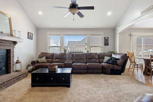 Living room with lofted ceiling, a brick fireplace, recessed lighting, and a ceiling fan