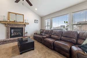 Carpeted living area featuring a fireplace, ceiling fan, and vaulted ceiling
