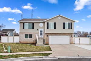 Bi-level home with driveway, a gate, fence, a garage, and brick siding