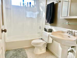Bathroom with tile patterned flooring, tub / shower combination, a wainscoted wall, toilet, and a sink