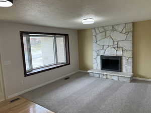 Unfurnished living room featuring visible vents, a stone fireplace, and baseboards