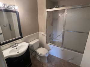 Full bathroom featuring shower / bath combination with glass door, toilet, vanity, and tile patterned flooring