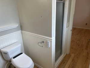 Bathroom featuring toilet, wood finished floors, a stall shower, and wainscoting