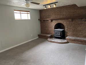 Unfurnished living room featuring baseboards, a wood stove, ceiling fan, a textured ceiling, and carpet flooring
