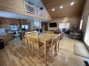 Dining room with log walls, visible vents, light wood finished floors, and high vaulted ceiling