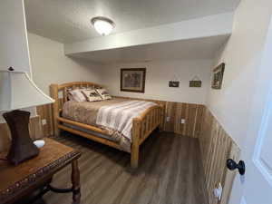 Bedroom with wood finished floors, wainscoting, wood walls, and a textured ceiling