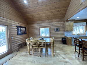 Dining room with wood ceiling, light wood-type flooring, high vaulted ceiling, and log walls