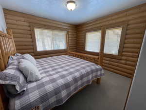 Bedroom with log walls, carpet floors, and a textured ceiling