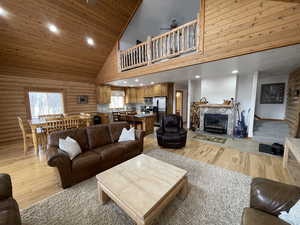 Living area with light wood-style flooring, a fireplace, high vaulted ceiling, and rustic walls